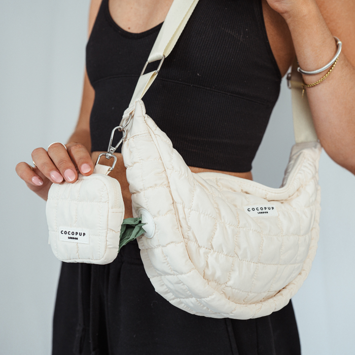 Woman in a black crop top holds a light grey Cocopup London crossbody dog walking bag with matching dispenser.
