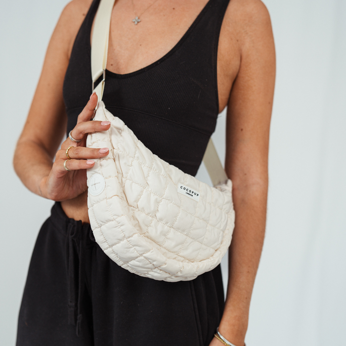 Woman in black tank top and pants holding a light-colored Cocopup London crossbody dog walking bag.