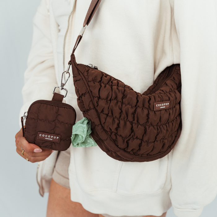 Person wearing an espresso brown Cocopup London crossbody crescent bag with matching pouch and visible poop bag.