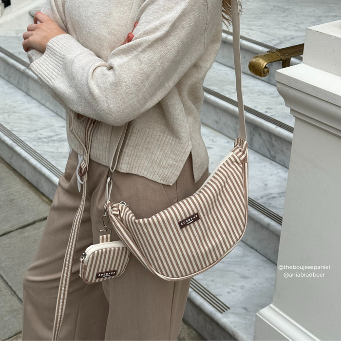 Person in a neutral outfit holding a linen-striped Cocopup London crossbody crescent dog walking bag bundle.