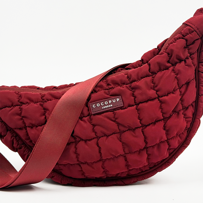 Merlot red crescent-shaped crossbody dog walking bag with wide strap and Cocopup London logo label on the front.