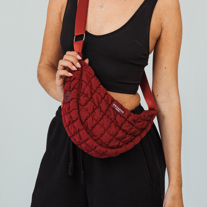 Person in black wearing a merlot Cocopup London crossbody crescent dog walking bag across their chest.