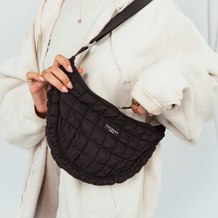 Person holding a black Cocopup London crossbody dog walking bag with built-in poop bag dispenser.