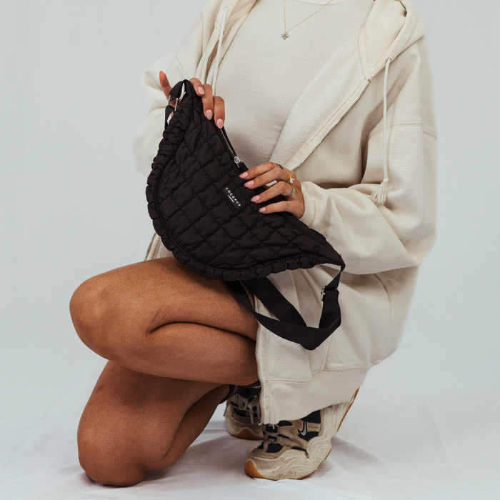 Person in beige hoodie holds black Cocopup London crossbody dog walking bag with attached dispenser.