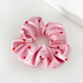 Pink scrunchie with red heart pattern on a white surface near the corner.