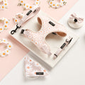 The Cocopup London Daisy Chain Adjustable Neck Harness, Lead & Collar Bundle includes a pink and white daisy pattern harness with an adjustable neck, leash, collar, bow tie, and bandana. Displayed on a marble surface with matching daisy decorations arranged around the items, this set ensures your pet's ultimate security with its safety lock feature.