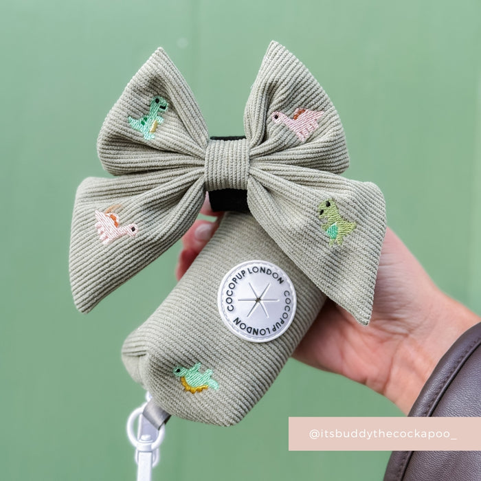 Sage green Cocopup London poop bag holder with bow, animal illustrations, and round label held in a hand.