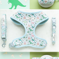 A light blue Dinopaws Adjustable Neck Harness, Lead & Collar Bundle by Cocopup London showcases a playful dinosaur print with various dinosaur illustrations, plants, and volcanoes. The brand name "Cocopup London" is clearly visible on both the harness and lead. The items are neatly arranged on a white surface.