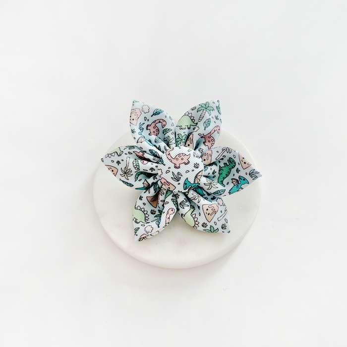Cocopup London Dinopaws Collar Flower with a colorful dinosaur print, shown on a round white surface.