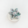 Cocopup London Dinopaws Collar Flower with a colorful dinosaur print, shown on a round white surface.