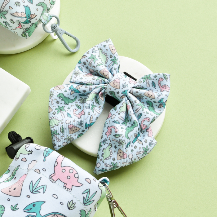 Pastel dinosaur-patterned Cocopup London sailor bow tie on a stand with a pale green background.