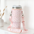 Pink tumbler with lid and straw inside a pink ditsy floral carry case, displayed on a white shelf.
