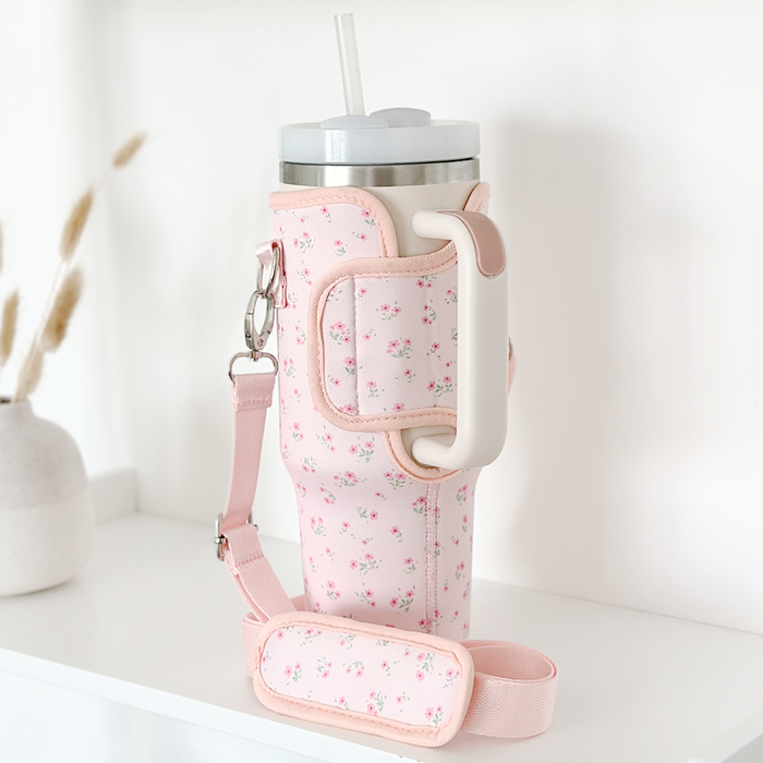 Pink floral Cocopup London tumbler in a matching Coconut Lane carry case on a shelf beside dried grass.