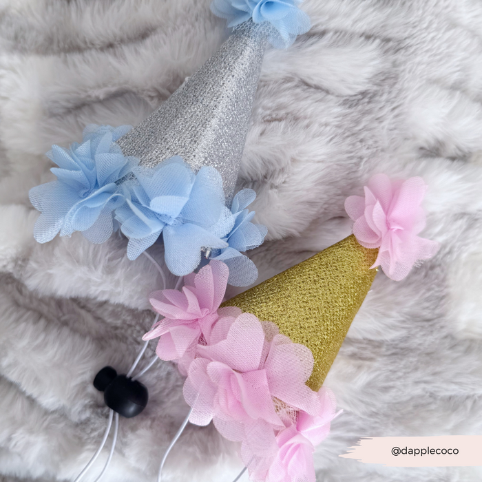Two pink Cocopup London dog party hats with tulle flower accents, displayed on a furry surface.