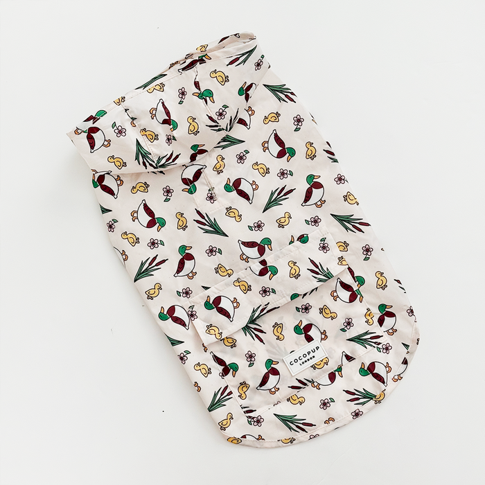 White Cocopup London dog raincoat with colorful bird and leaf print, features a pocket detail.