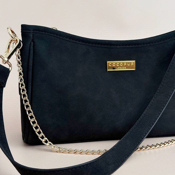 Black suedette dog walking bag with gold chain strap, front label, and built-in poop bag dispenser.
