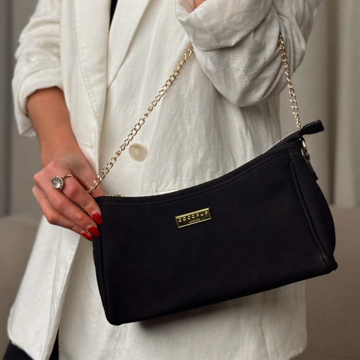 Black suede Cocopup London Dog Walking Bag with gold chain strap and poop bag dispenser, held by a person in a white blazer.