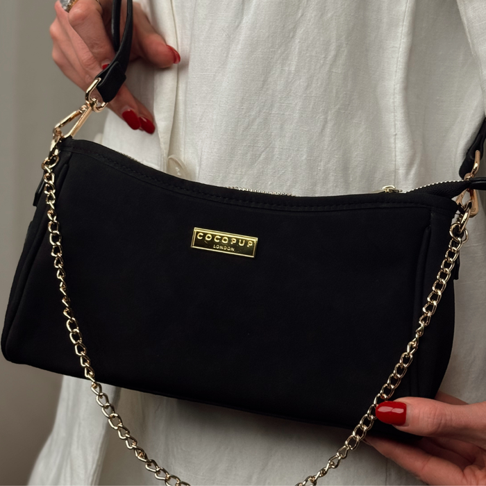 Woman in a white dress holding a black suedette Cocopup London dog walking bag with a gold chain strap.