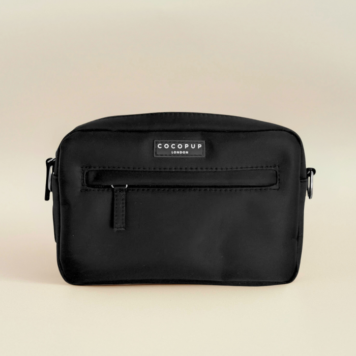 Small black Cocopup London dog walking bag with front zipper and poop bag dispenser on a beige background.