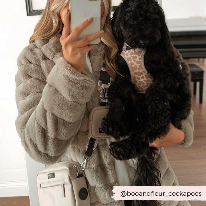 Woman in beige faux fur coat takes mirror selfie; her black dog wears a caramel tan Cocopup London dog walking bag.