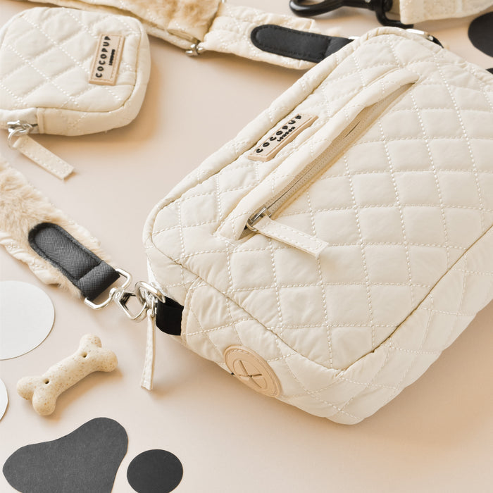 Cream quilted dog walking bag set with matching harness, lead, and poop bag dispenser on a beige background.