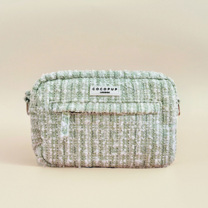 Light green and white textured tweed dog walking bag with front pocket and logo, shown on a beige background.