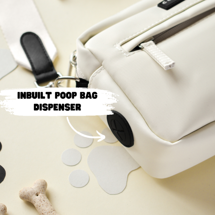 Oyster white Cocopup London dog walking bag with labeled poop bag dispenser, shown among assorted dog accessories.