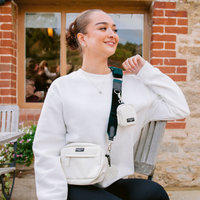 Woman in a white sweater sits outdoors with two Oyster White Cocopup London Dog Walking Bags.