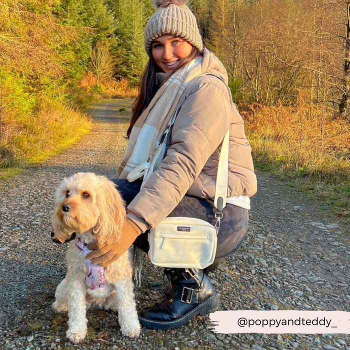 Woman kneels by her dog on a forest path, holding an oyster white Cocopup London dog walking bag.