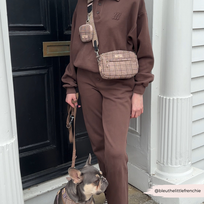 Person in brown outfit with French bulldog in matching harness, holding leash and plaid Cocopup London dog walking bag.