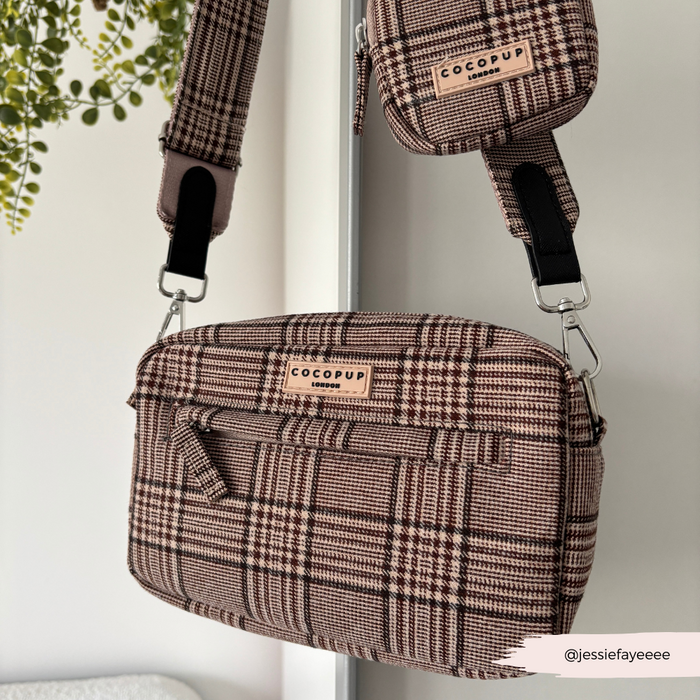 Plaid Cocopup London dog walking bag with treat pouch hanging on a white hook beside green leaves.