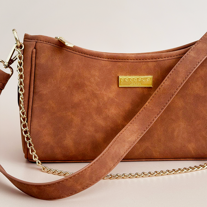 Tan suedette dog walking bag with gold chain strap, logo plate, and front dispenser for poop bags.