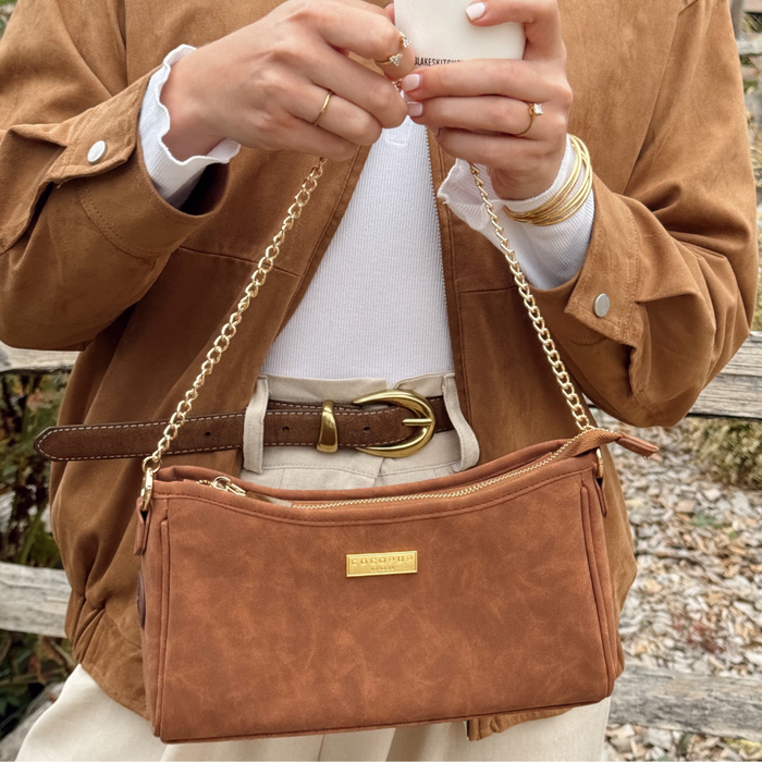 Cocopup London Tan Suedette Dog Walking Bag with gold chain, held by person in brown jacket and beige pants.