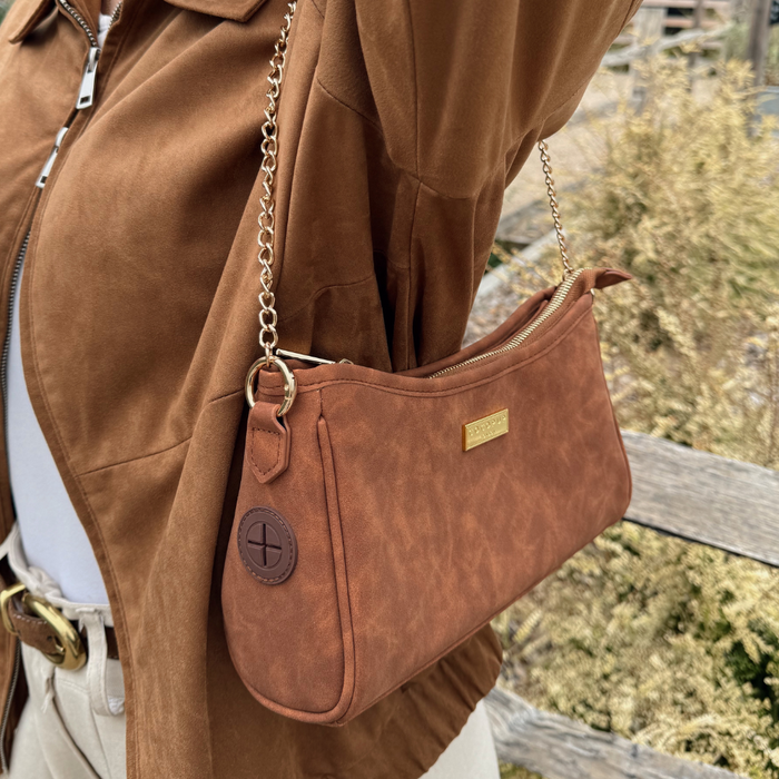 Person holding a tan suedette Cocopup London dog walking bag with gold chain strap.
