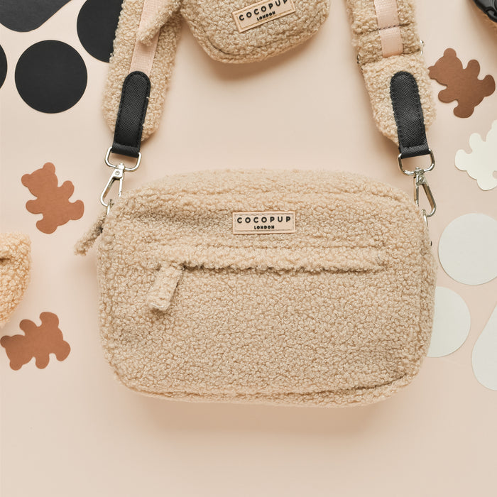 Beige sherpa dog walking bag by Cocopup London on cream surface with black and brown abstract shapes.