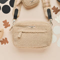 Beige sherpa dog walking bag by Cocopup London on cream surface with black and brown abstract shapes.
