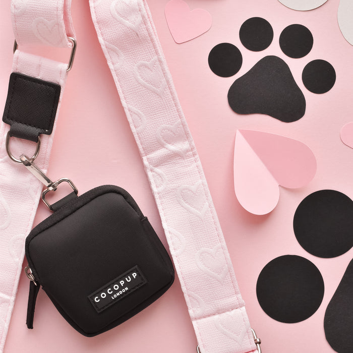 Baby pink Cocopup London dog walking bag with heart detail, black poop bag dispenser, and paw print on pink background.