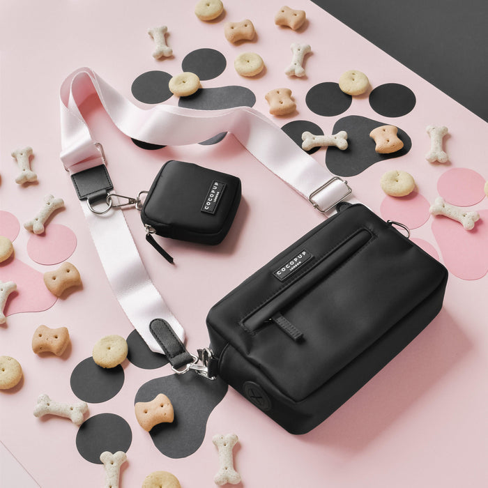 Baby pink Cocopup London crossbody dog walking bag and treat pouch with matching pink strap on a pink and black background.