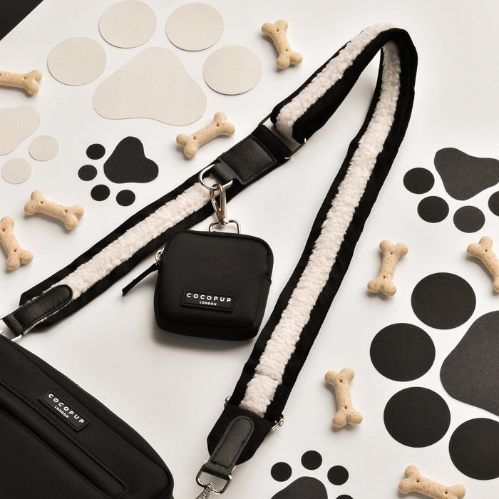 Black Aviator dog walking bag with matching treat pouch, displayed among dog treats and paw print cutouts.