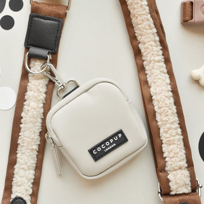 Brown Aviator Cocopup London dog walking bag with fluffy strap on a light surface with scattered shapes.