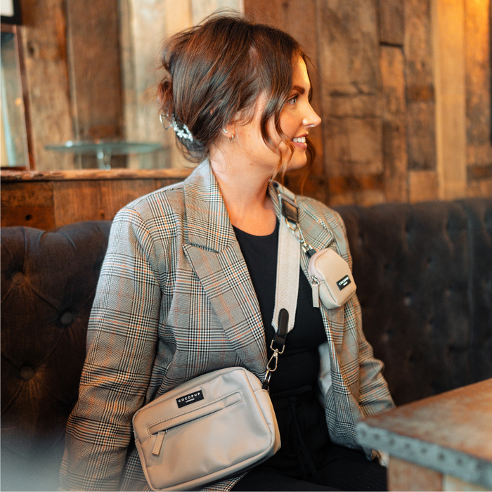 Woman in a plaid blazer sits on a bench with the brown tweed Cocopup London Dog Walking Bag Bundle.