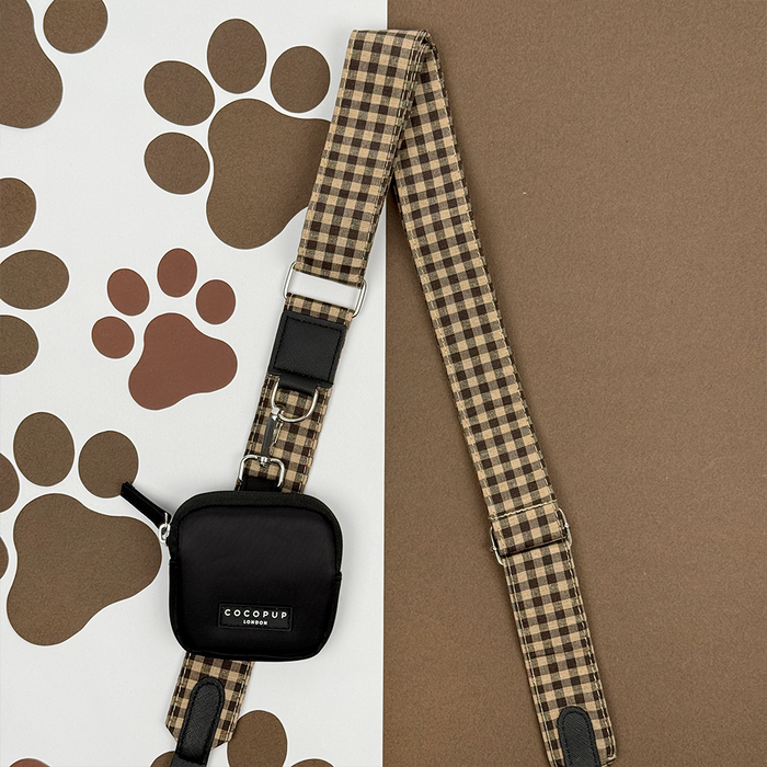 Cocopup London dog walking bag with a black pouch and checkered strap, shown on a paw print background.
