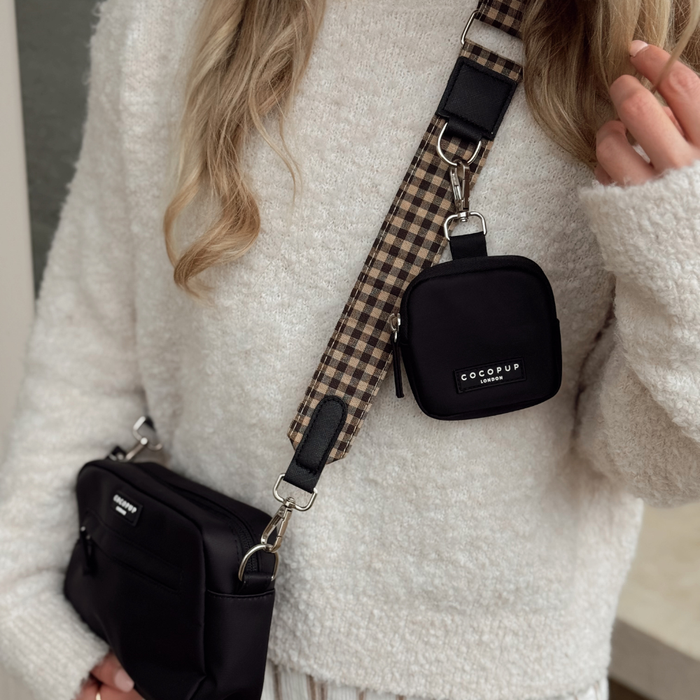 Woman in a white textured sweater carries two black bags with a Cocopup London Cotswold Check bag strap.