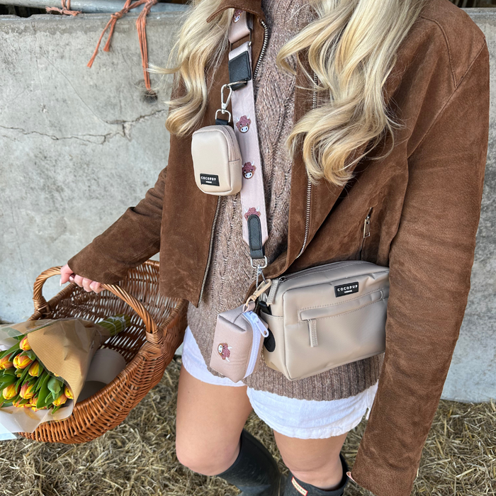 Woman in a brown suede jacket holds flowers, wearing a brown Cocopup bag strap with a cow design.