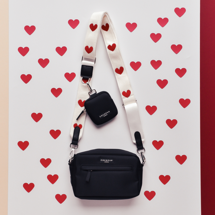 Black Cocopup London crossbody bag with case and Hugs & Knitted strap, shown on a white background with red hearts.