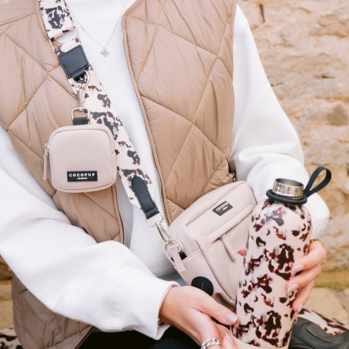 Woman in a beige vest holds an ivory Cocopup London dog walking bag with matching treat pouch and poop bag dispenser.