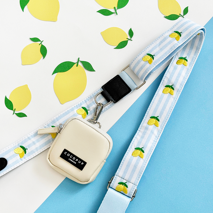 Oyster white dog walking bag with a lemon yellow strap, displayed on a yellow and blue background.