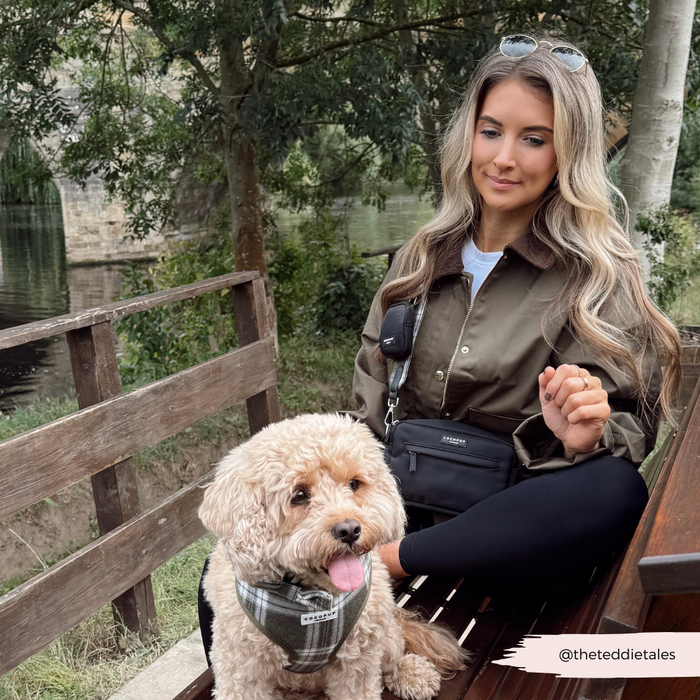 Woman by the water with a fluffy dog in a plaid harness and olive check Cocopup London dog walking bag.