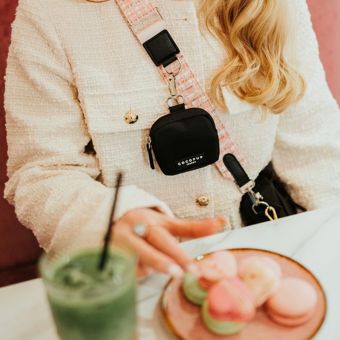 Pink textured tweed Cocopup London bag strap on white table next to colorful macarons and a womans hand reaching.
