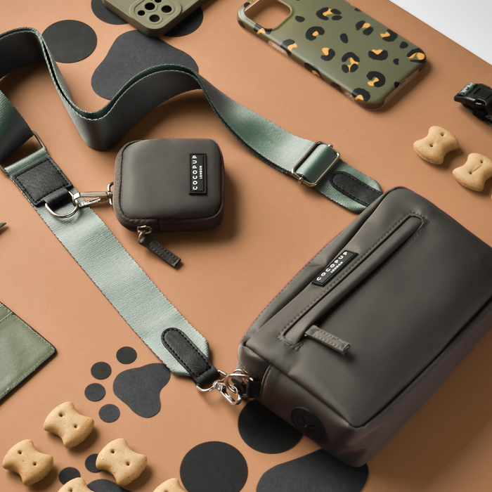 Khaki dog walking bag set with matching treat pouch, dispenser, and green strap on a brown background.